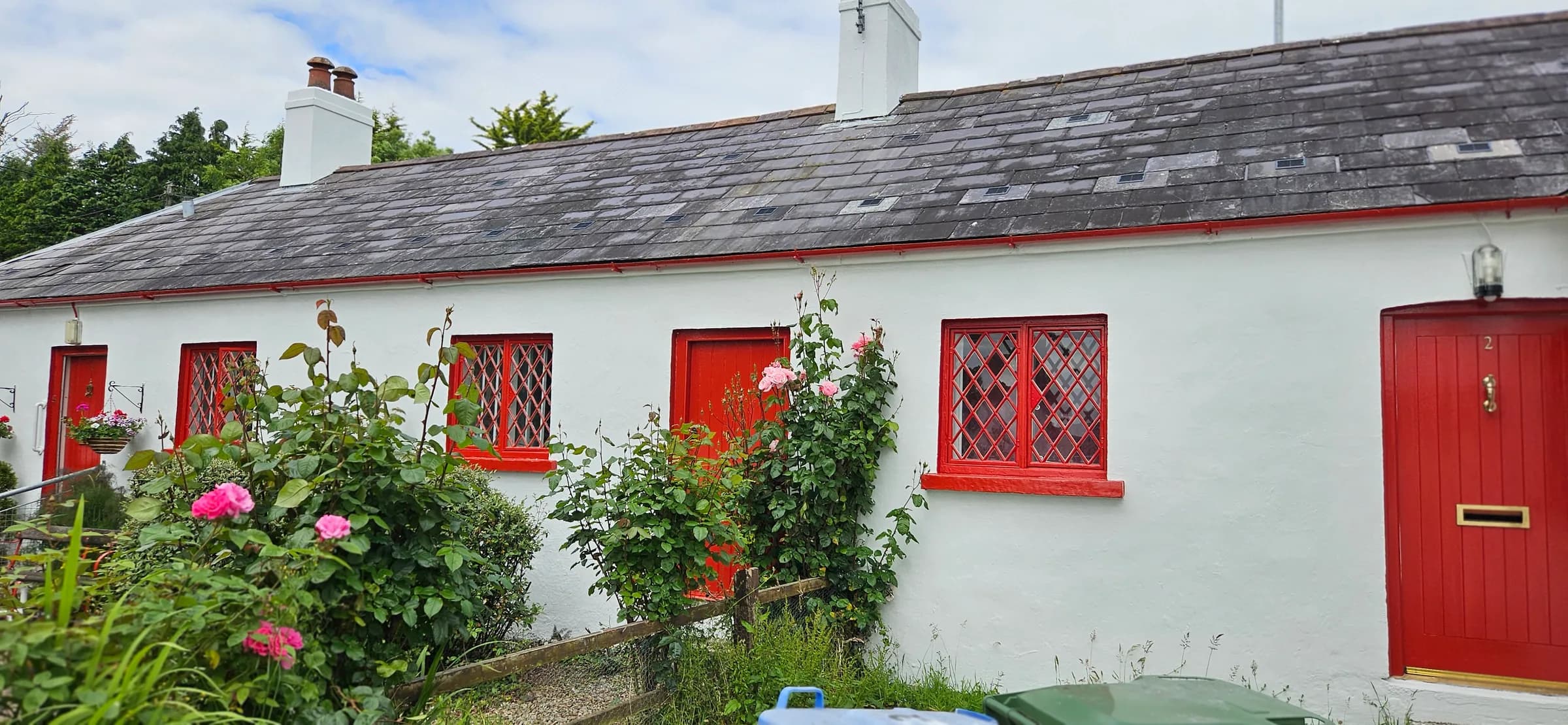 Whitewashed cottage with red doors and red diamond-leaded windows, pink roses climbing the front wall