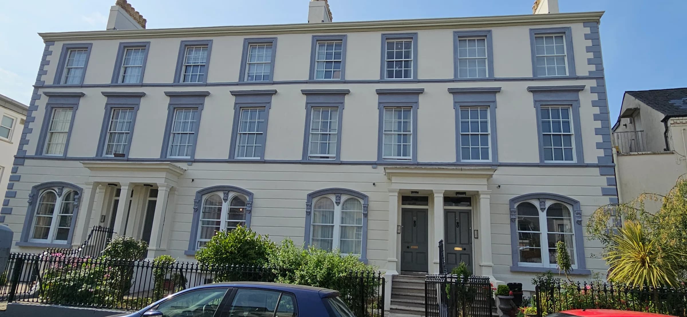 A three-storey rendered terrace painted cream with blue-grey picked-out window surrounds, quoins and cornice, sash windows above arched ground-floor windows