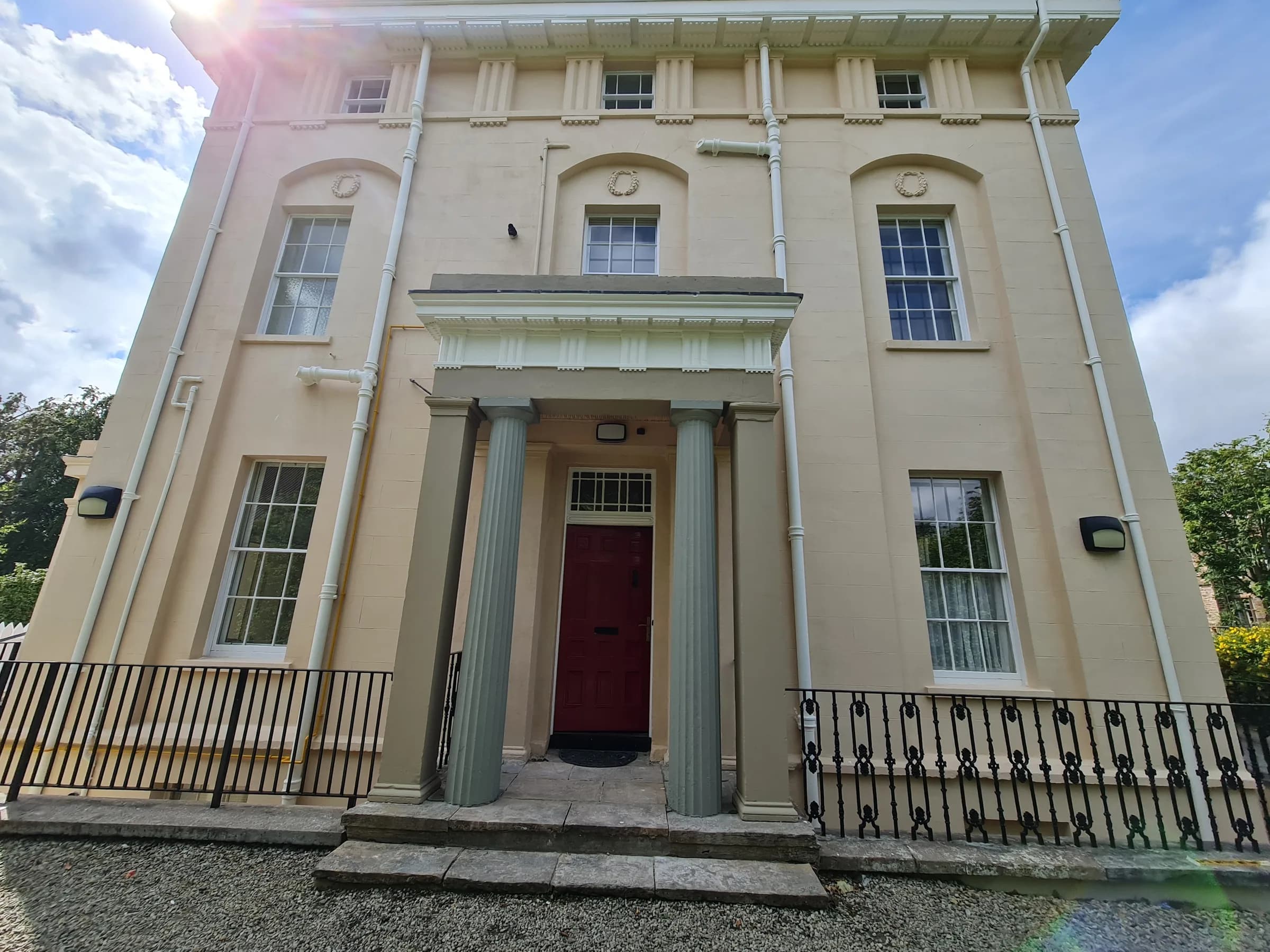 Georgian villa with a sage-grey columned portico, a red front door, white sash windows and black railings