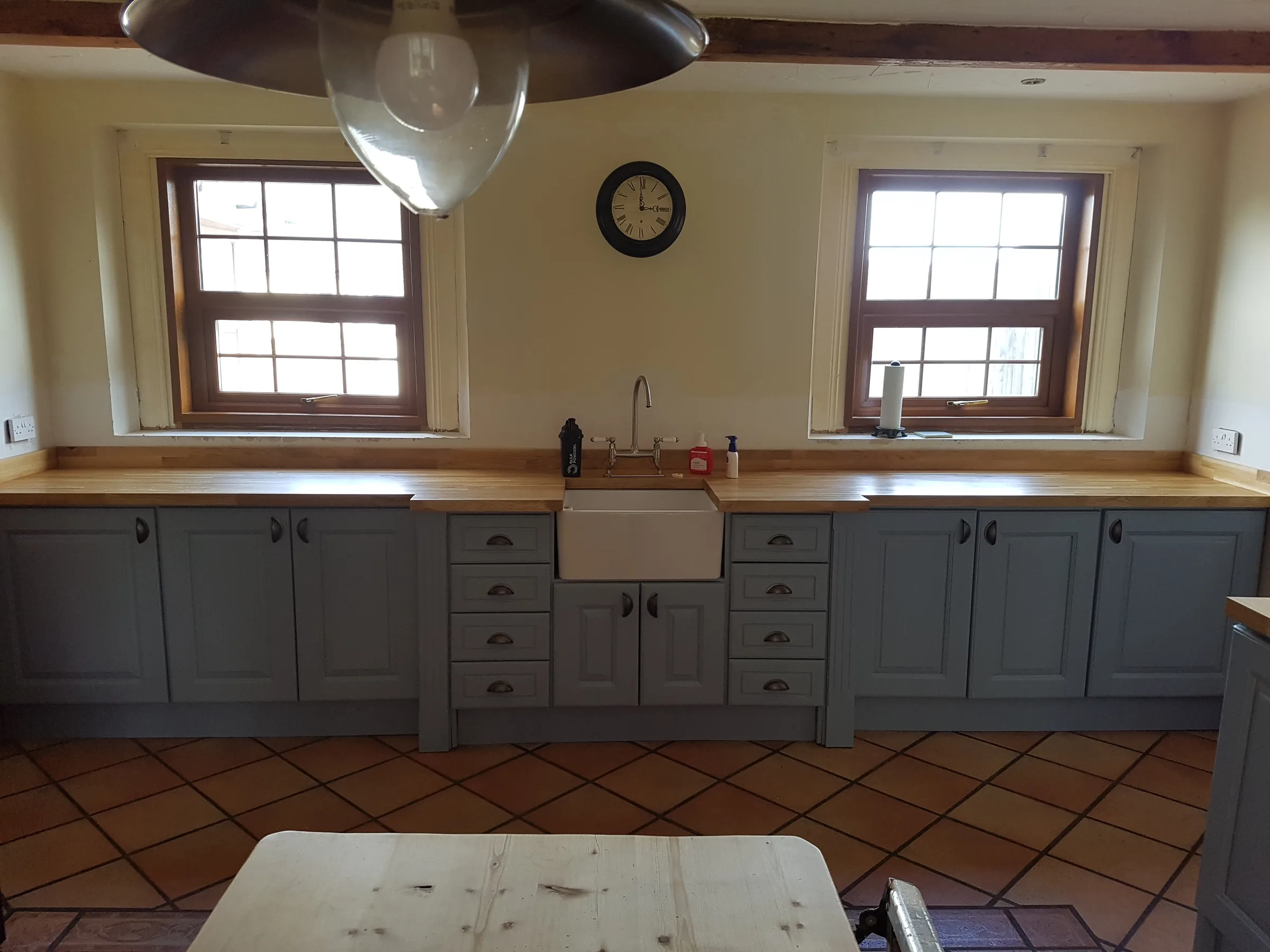 Farmhouse kitchen with blue-grey raised-panel cabinets, a Belfast sink, a solid wood worktop and a terracotta tiled floor