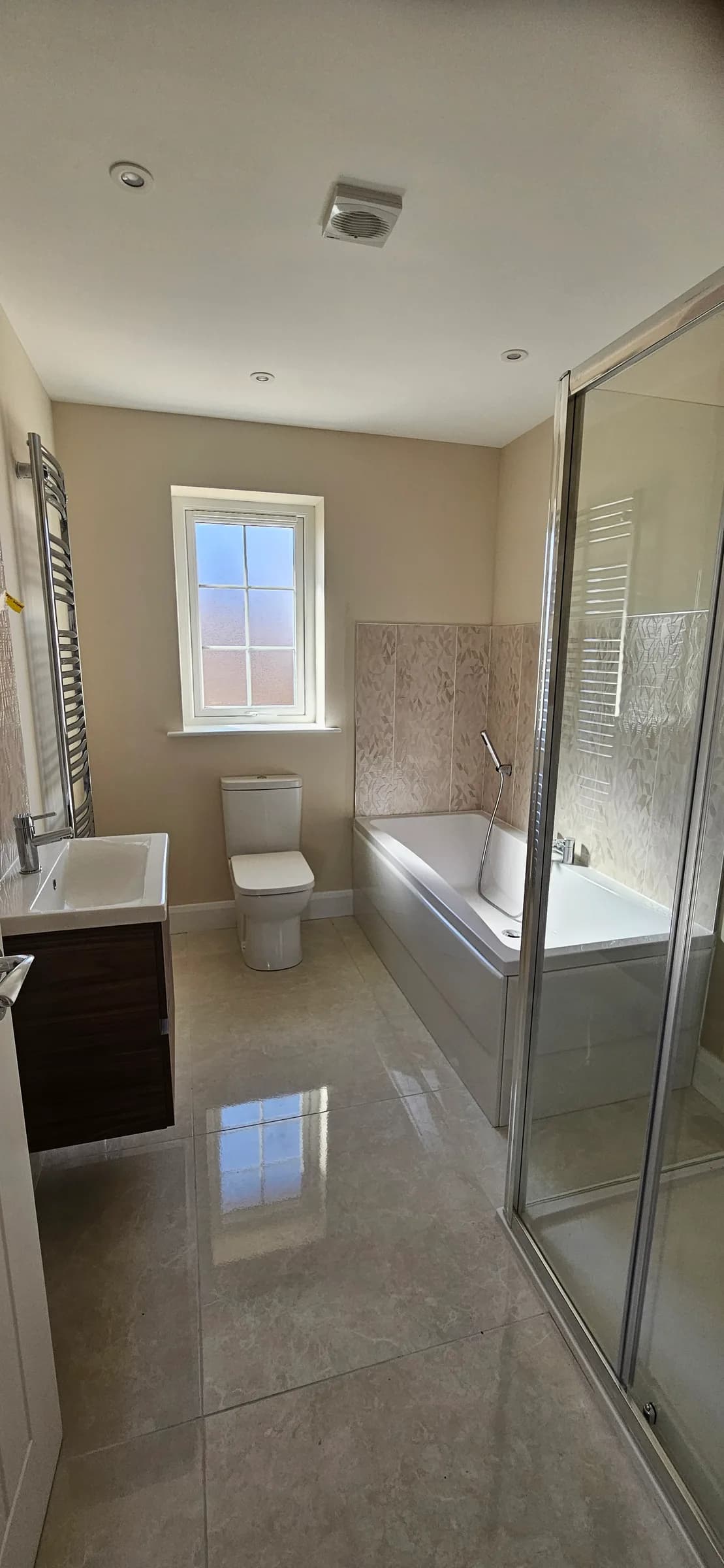 Bathroom with a bath and shower screen, white WC and a basin on a dark vanity unit, with a polished tiled floor