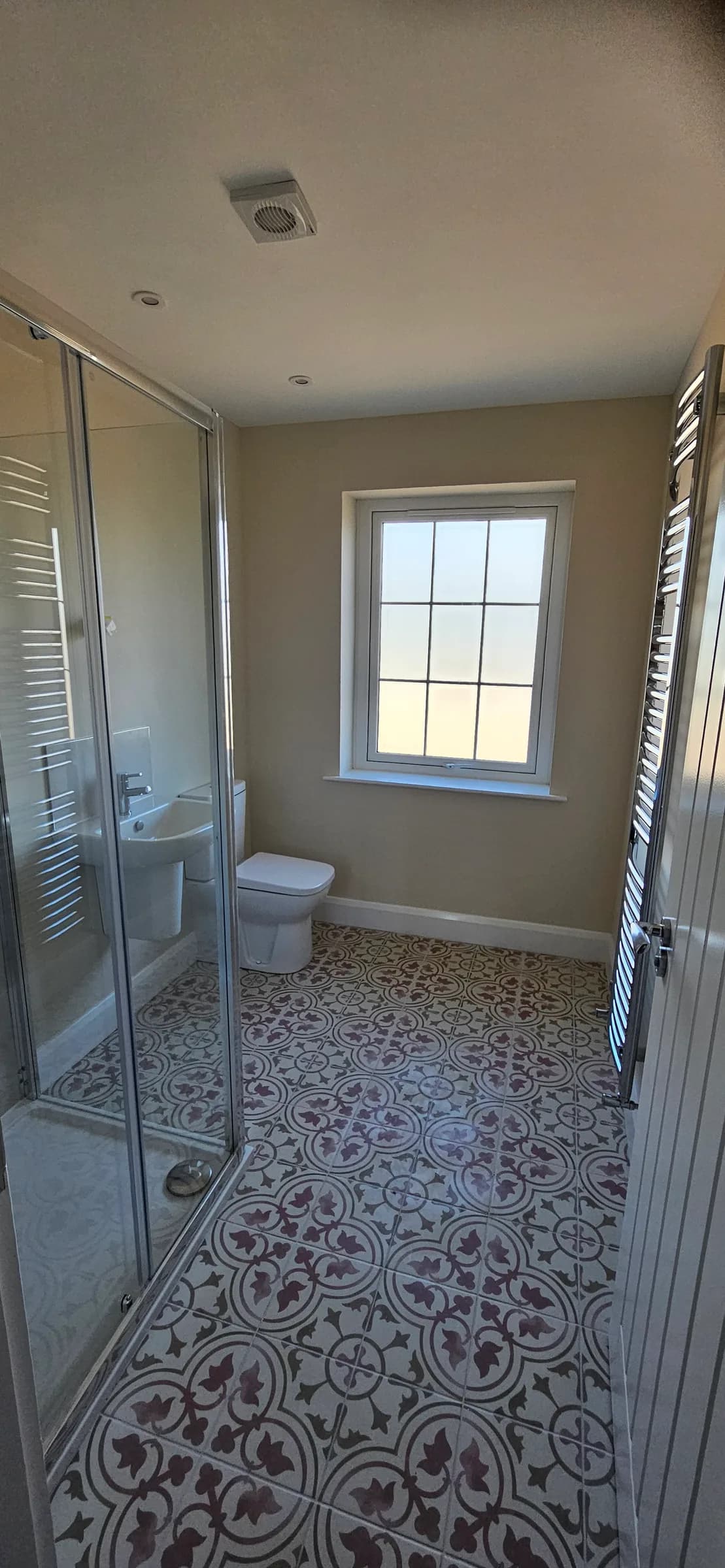 Shower room with a glass enclosure, white WC and basin, and a patterned grey and burgundy tiled floor