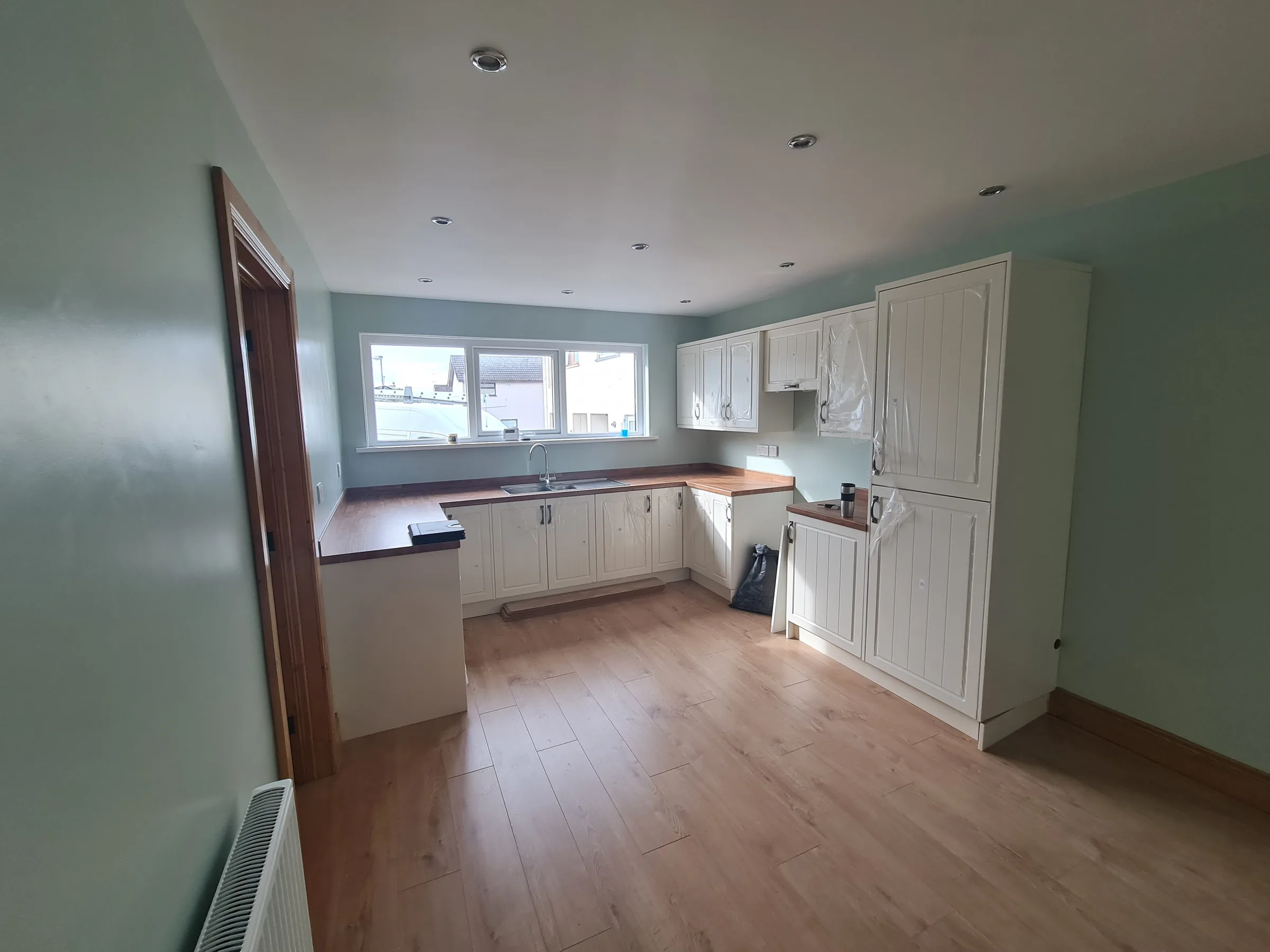 Open-plan kitchen diner with soft green walls, cream panelled units, wood-effect worktops and a laminate floor