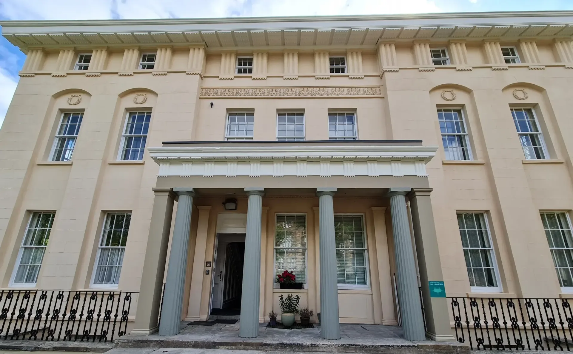 Georgian villa at Clifton Villas, Belfast — cream rendered facade, four sage-grey fluted columns supporting a white portico, and an open front door behind them.