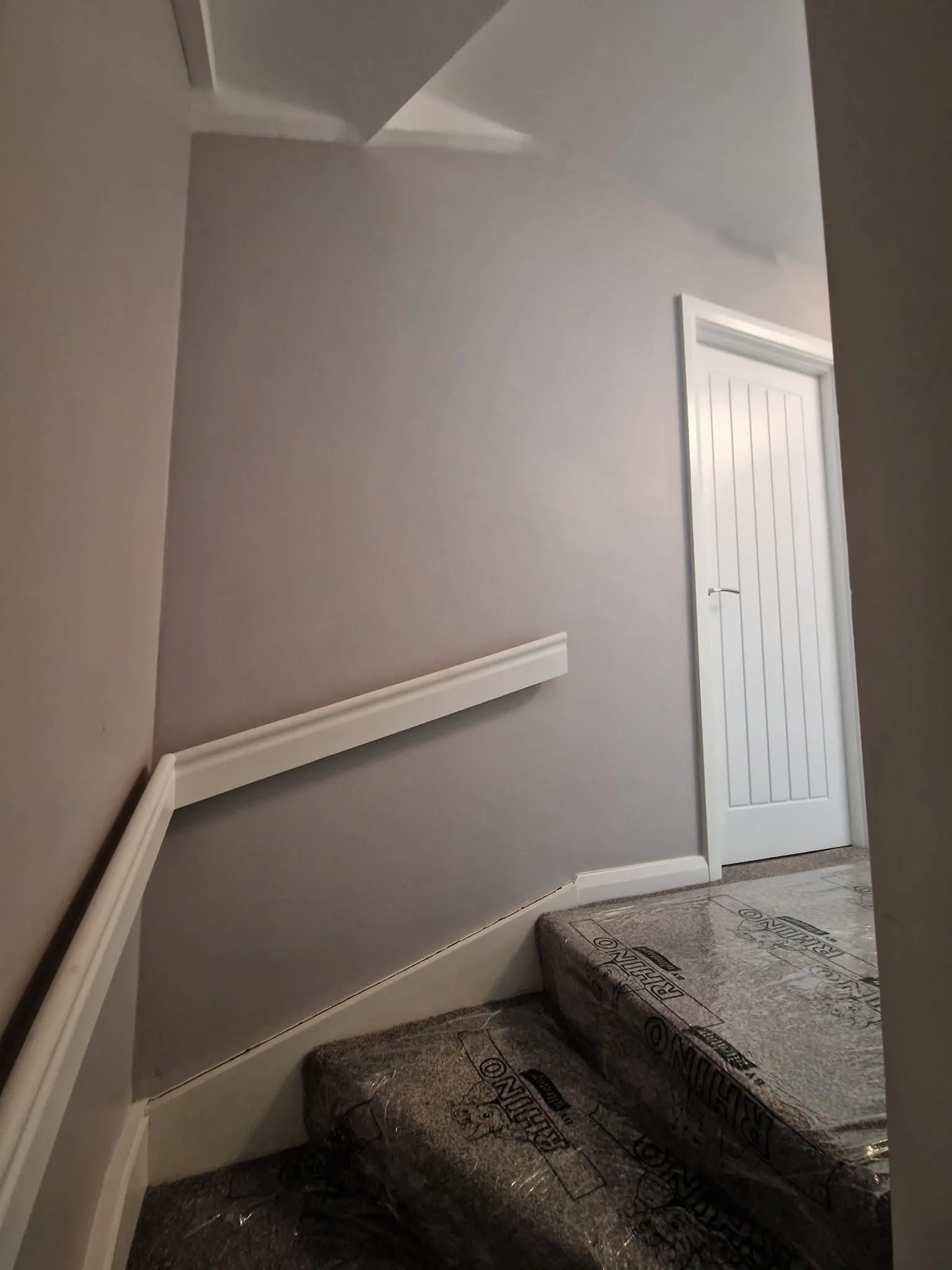 Self-adhesive Rhino carpet protection taped down over a stairway and landing, with freshly painted grey walls, white dado rail and white skirting