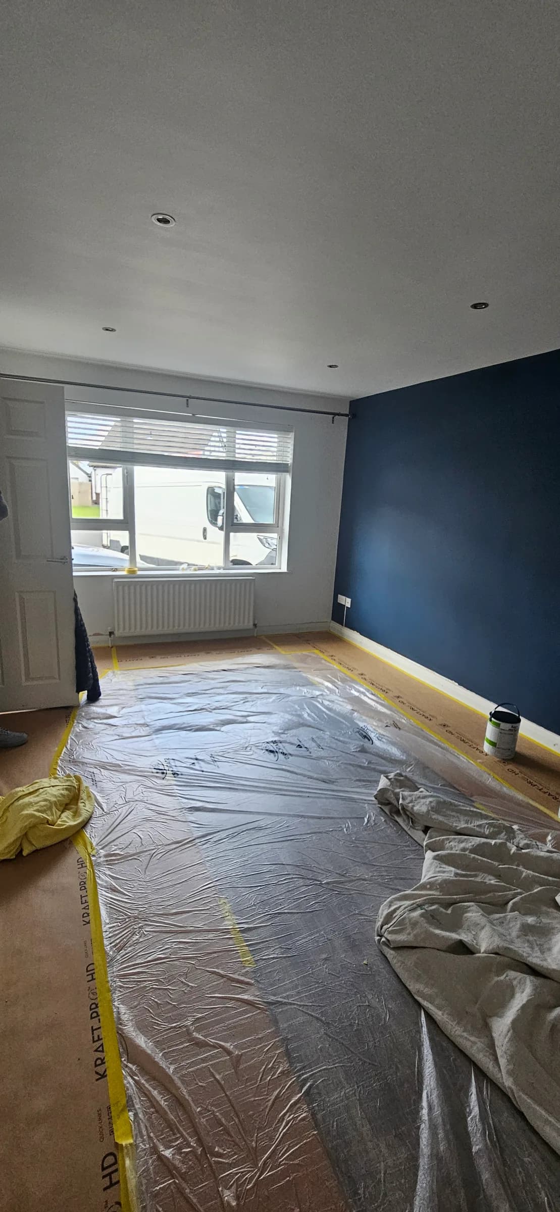A room with a freshly painted deep navy wall, the floor covered with Kraft-Pro paper and plastic sheeting taped along the edges