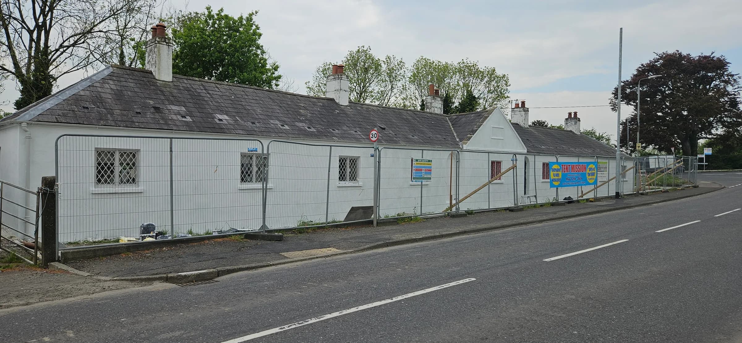 The same terrace mid-programme, site fencing and contractor boards in place along the road