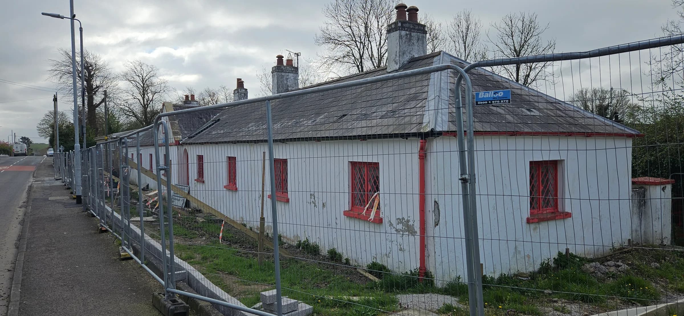 End elevation of the terrace before work, render weathered, groundworks and site fencing in front