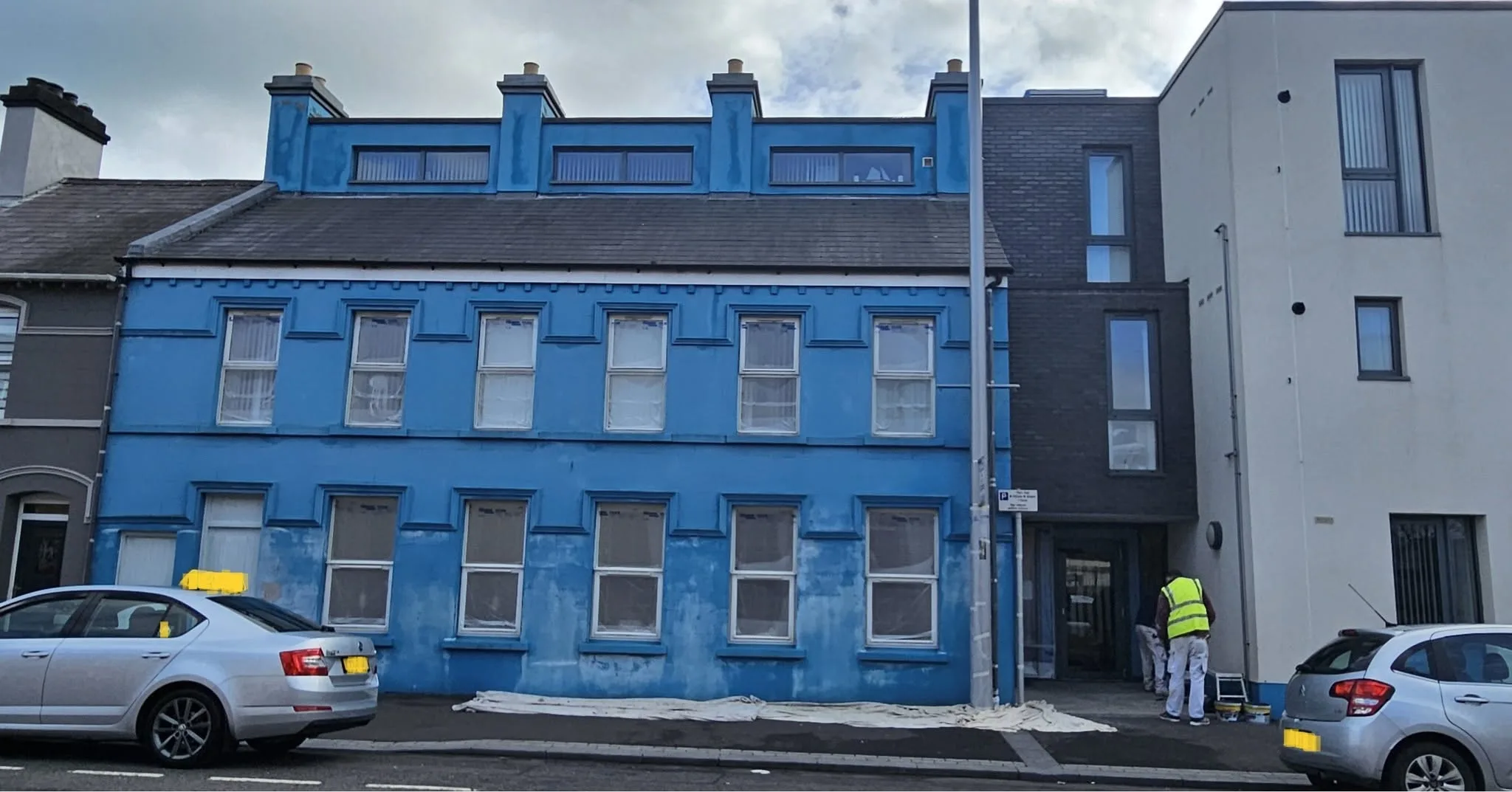 Rendered Victorian terrace painted blue, the finish patchy and weathered, with a dust sheet laid along the footpath