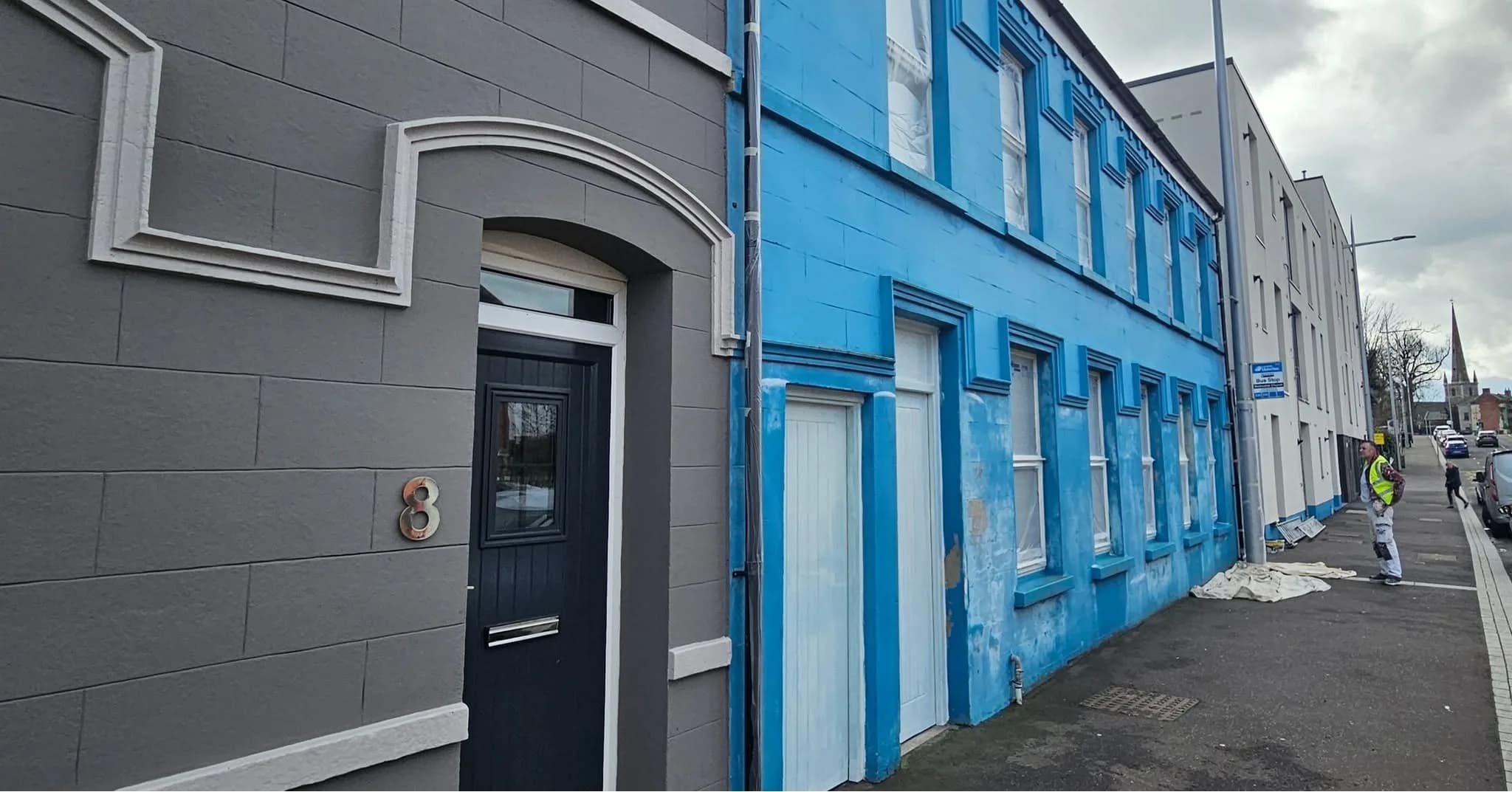 Grey-rendered end house with a black front door, the weathered blue terrace running away down the street
