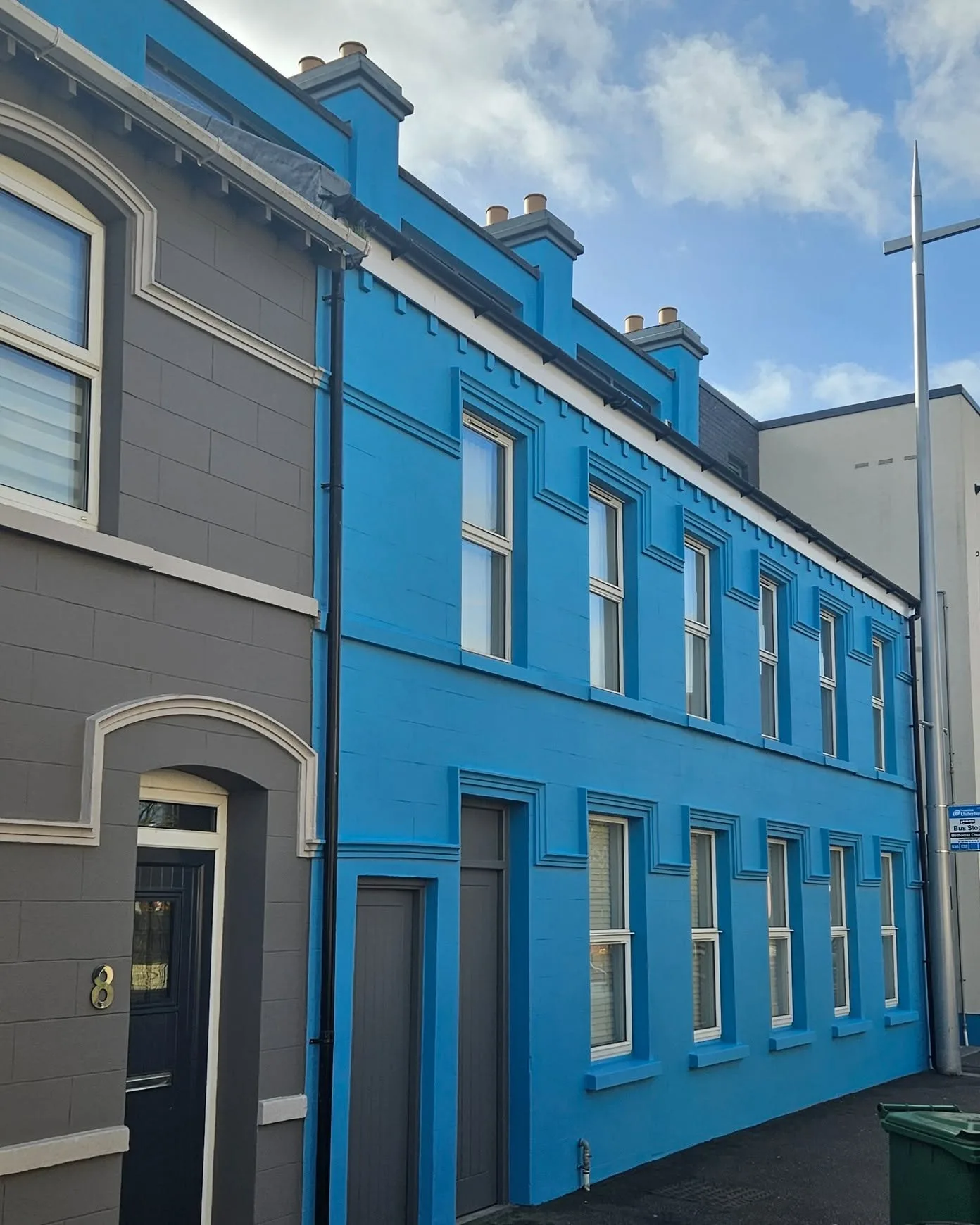 The finished terrace from the corner, grey end house with a black front door beside the repainted blue frontage