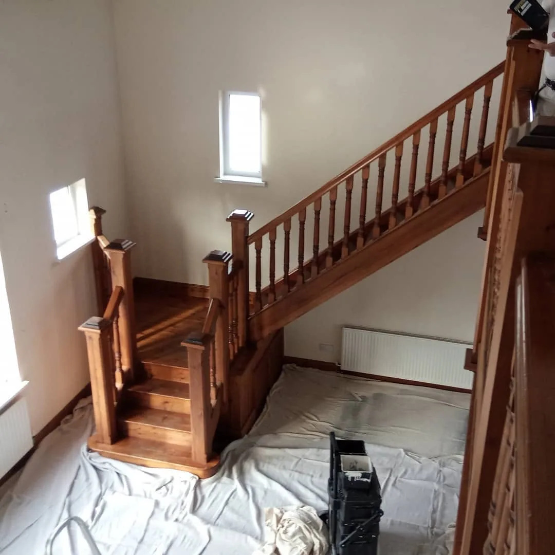 Varnished pine staircase with turned spindles and newel posts, dust sheets laid over the floor below