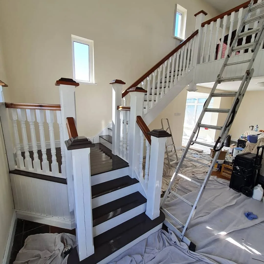 The same staircase part-painted, spindles and newel posts in white with the treads stained dark, a ladder and tool chest alongside