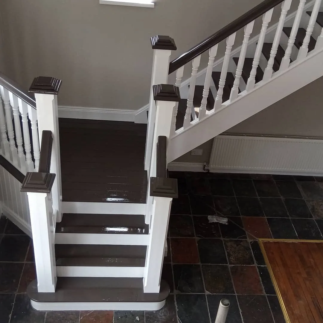 The finished staircase with white spindles and newel posts, dark stained treads and handrail, on a slate floor